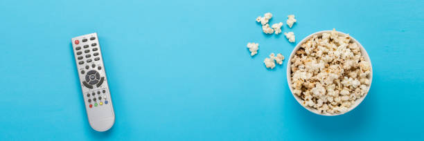 istock Bowl with popcorn and remote control for TV on a blue background 1253993253