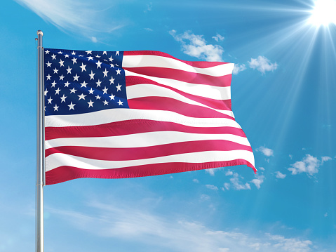 United States national flag waving in the wind against deep blue sky. High quality fabric. International relations concept.