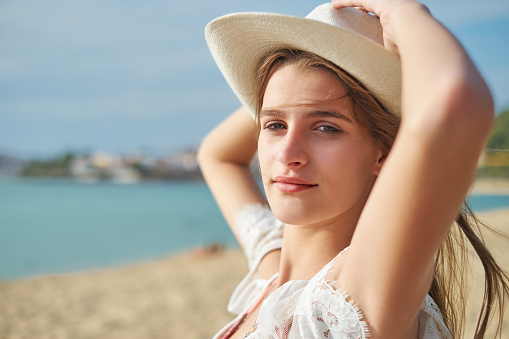 Portrait of a young natural beauty standing on the beach, holding straw hat and looking at camera, copy space