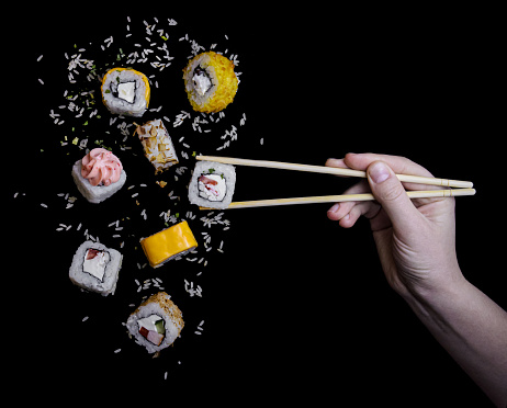 flying up sushi california alaska lava chidder together with rice on a black background close-up with bamboo sushi sticks gripping them