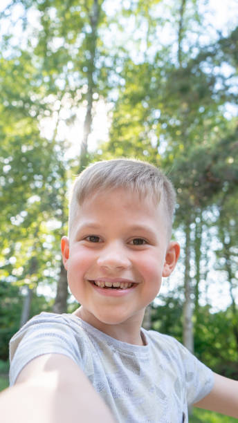 istock Authentic Funny small boy taking selfies and laughing. Smiling cute boy taking photos and facetime chatting with family. Vertical photo. 1253997519