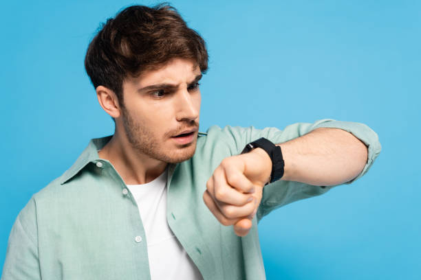 istock shocked young man looking at wristwatch isolated on blue 1253998243