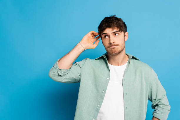 istock thoughtful young man looking away and touching head on blue 1253998252