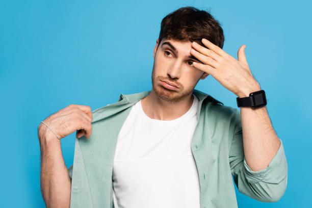 istock displeased young man touching forehead while suffering from summer heat isolated on blue 1253998281