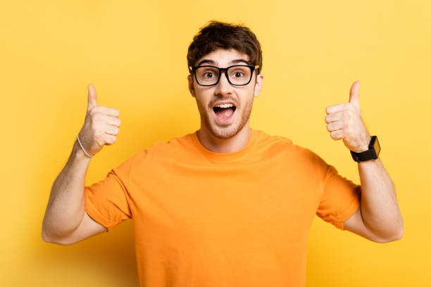 istock excited young man showing thumbs up while looking at camera on yellow 1253998283