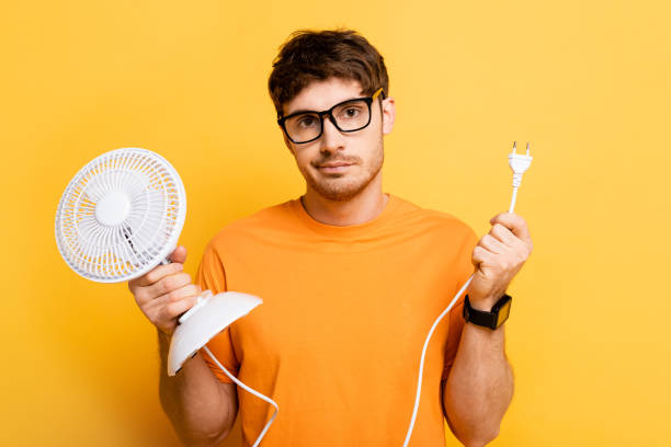 istock disappointed young man holding electric fan while looking at camera on yellow 1253998288