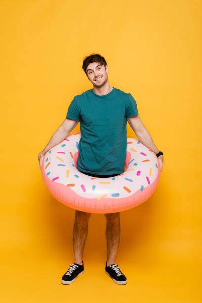 istock smiling man standing with inflatable donut on yellow 1253998314
