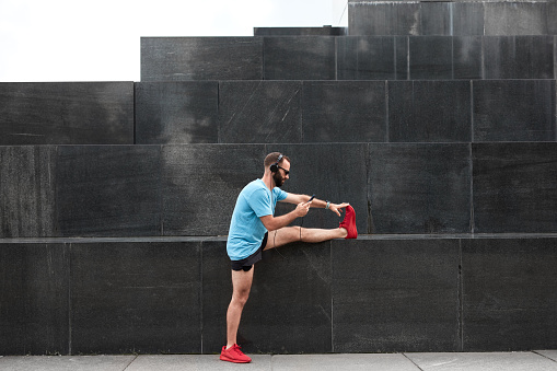 Modern sporty man making pause and stretching after jogging / exercise in urban environment.