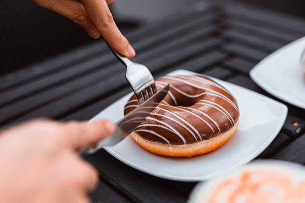 istock Close up of hands with fork and knife cutting donut shape. 1254010594
