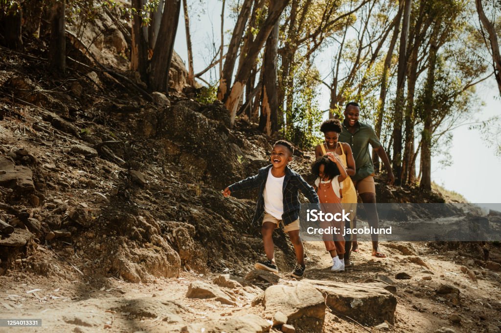 Family running down rocky trail Young family running down rocky mountain trail. Two kids running with parent on a trail in forest. Family Stock Photo