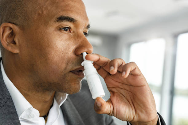 Mid adult African American man using nasal spray. Black entrepreneur using nasal spray for his illness in the office. nasal spray stock pictures, royalty-free photos & images