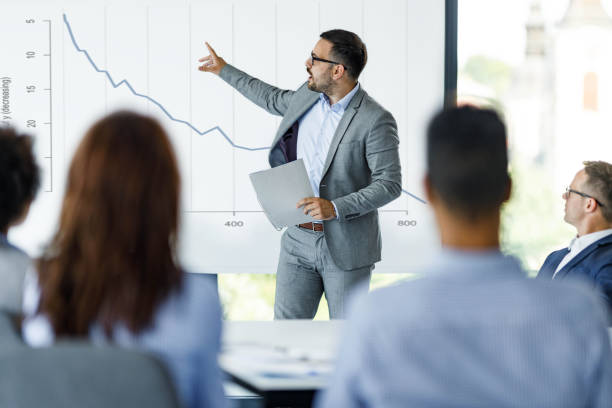 Male CEO talking about economic crisis on presentation in the office. Young male leader giving his colleagues a presentation about economic depression in the office. moving down photos stock pictures, royalty-free photos & images