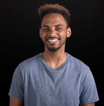Portrait of smiling young man in grey t-shirt against black background.