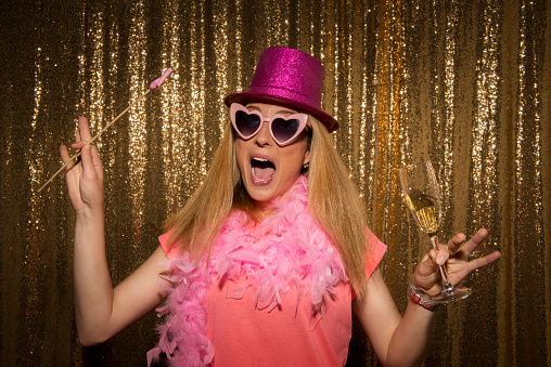 Portrait of mid adult woman in pink top wearing heart shaped sunglasses and holding a flute of champagne with disguise.