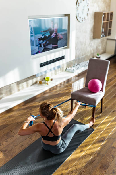 istock Athletic woman exercising with elastic rope during online exercise class at home. 1254016103