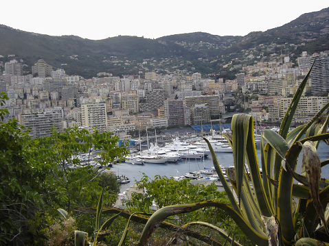 An aerial view of the cityscape of Monaco and the harbor filled with yachts on a sunny day