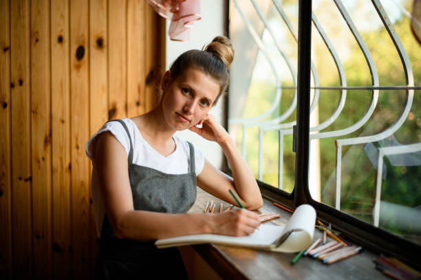 istock handsome young woman standing by window and looks at camera 1254025722