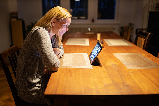 Smiling woman having a video call on her digital tablet. Woman talking with colleagues over a video conference.