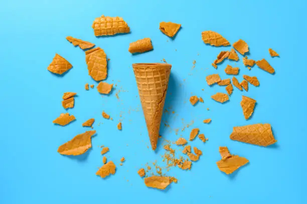 an intact ice cream cone surrounded by broken fragments on blue background