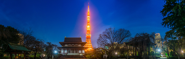 The iconic spire of the Tokyo Tower spotlit against chrome blue dusk skies overlooking the historic temples of the Zojoji Shrine and skyscraper skyline of central Tokyo, Japan’s vibrant capital city.