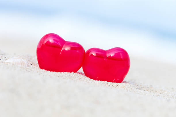 Red decoration hearts on sandy beach with sea background,  shallow depth. Valentines day card and love to travel concept