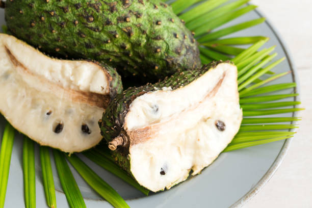 Tropical fruit Guanabana on plate Closeup of green soursop graviola, exotic, tropical fruit Guanabana on plate decorated palm leaves. Alternative medicine treatment of cancer green apple slice overhead stock pictures, royalty-free photos & images