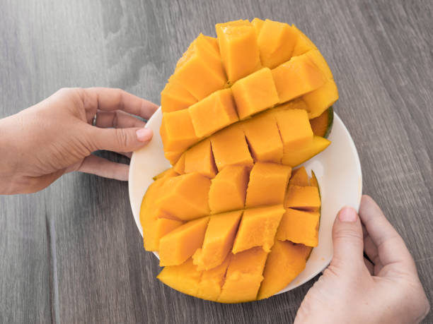 istock Half cutted cubes slices ripe mango on white plate in hands 1254034681