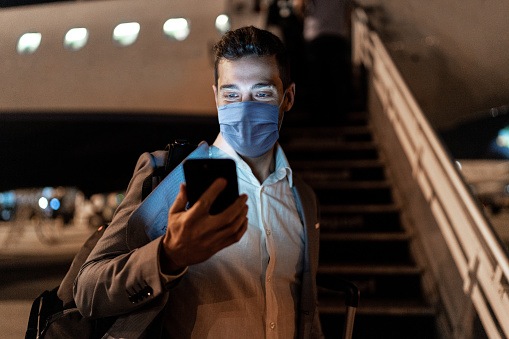 Businessman using mobile phone at airport using protective mask