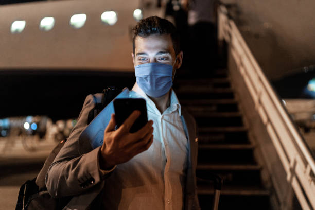 бизнесмен с помощью мобильного телефона в аэропорту с помощью защитной маски - airplane smart phone travel mobile phone стоковые фото и изображения