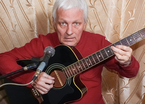 Senior man sitting with a guitar recording a track in a home studio