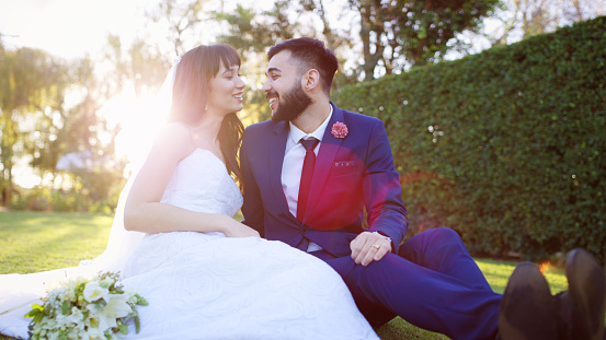 Shot of a happy young couple sitting on the lawn after getting married in a garden