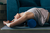 Working Out at Home: Woman is Sportswear Using a Roller to Massage Back Muscles