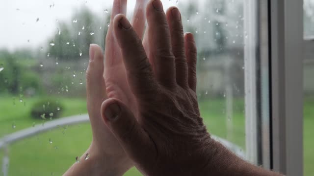 Woman And Old Man Touch Palms Of Their Hands Through Glass Window Closeup