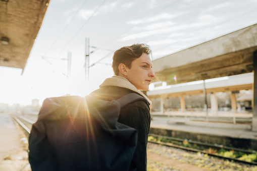 Photo of a young man standing on railroad station while waiting for a train