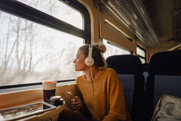 Young woman riding a train Photo of a young woman riding on a train, enjoying her trip while looking through the window and listening to some music on her mobile phone fall travel stock pictures, royalty-free photos & images