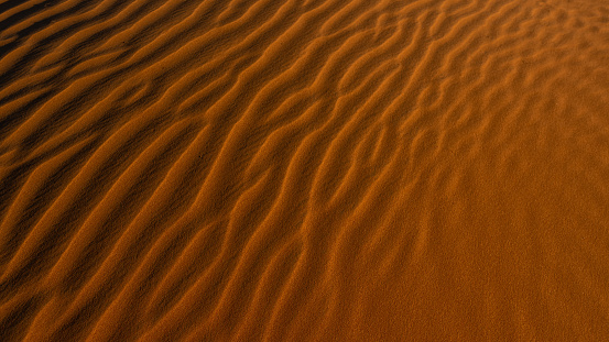 Red sand background with shadows from sunset sun, shot in desert at summer evening. Tourist attraction.