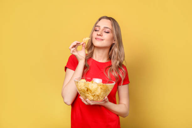 красивая женщина с чипсами на желтом фоне - potato chip стоковые фото и изображения