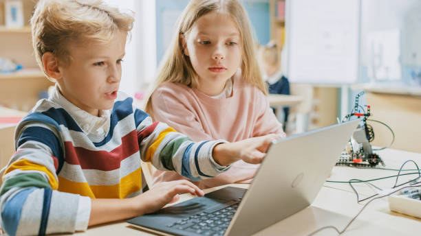 istock Brilliant Schoolgirl and Schoolboy Talk and Use Laptop to Program Software for Robotics Engineering Class. Elementary School Science Classroom with Children Working on Technology. STEM Education 1254050826