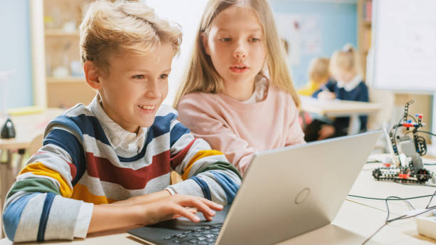 istock Brilliant Schoolgirl and Schoolboy Talk and Use Laptop to Program Software for Robotics Engineering Class. Elementary School Science Classroom with Children Working on Technology. STEM Education 1254050834