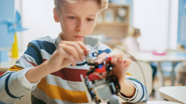 スマートな男子生徒のポートレートショットは、ロボット工学クラスのための小型ロボットを構築します。技術を持つ才能ある優秀な子供たちと小学校の科学教室 - elementary school building ストックフォトと画像