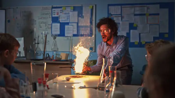 Photo of School Chemistry Classroom: Engrossed Children Watch How Enthusiastic Teacher Shows Science Experiment by Setting Powder on Fire Creating Beautiful Fireworks. Kids Getting Fun Modern Education