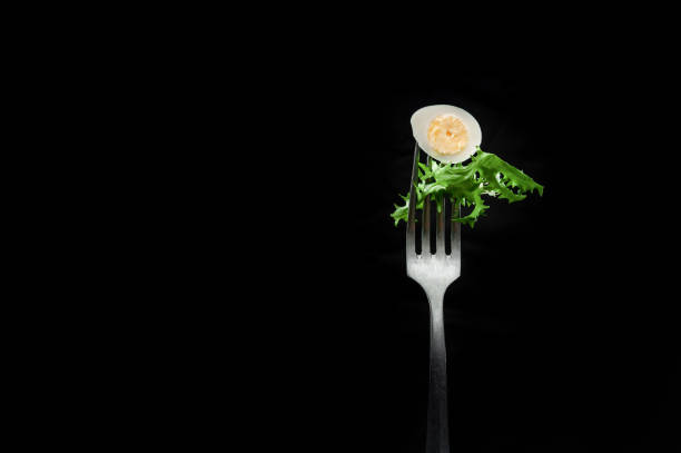 istock Quail egg with salad on a fork on a black background 1254052537