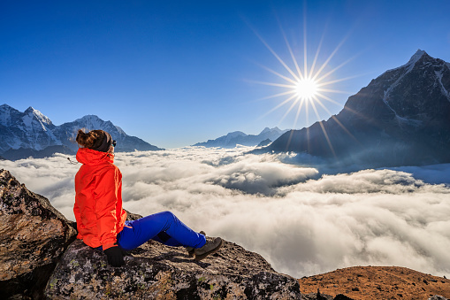 Young woman, wearing red jacket, is sitting on the top of a mountain and watching sunset over Himalayas .Mount Everest National Park. This is the highest national park in the world, with the entire park located above 3,000 m ( 9,700 ft). This park includes three peaks higher than 8,000 m, including Mt Everest. Therefore, most of the park area is very rugged and steep, with its terrain cut by deep rivers and glaciers.