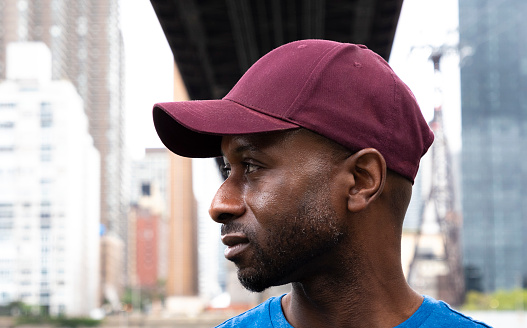 Portrait of a dark male sporter under a bridge in downtown New York.He's wearing a cap and has a white towel around his neck.