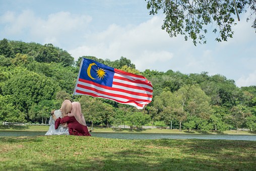 Happy young women in hijab holding Malaysian flag during Malaysia Merdeka Day