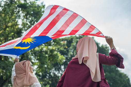 Happy young women in hijab holding Malaysian flag during Malaysia Merdeka Day