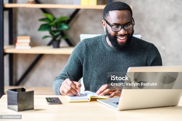 An Africanamerican Guy Using Laptop In The Office Stock Photo - Download Image Now - Men, Laptop, Web Conference