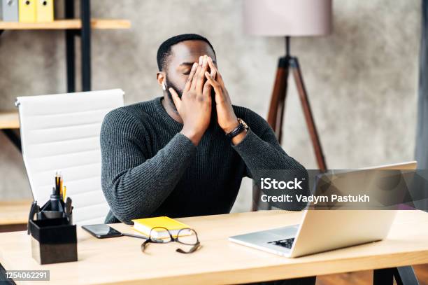 Tired Africanamerican Sits At The Desk Stock Photo - Download Image Now - Frustration, Anger, Laptop