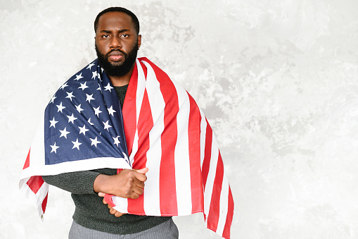 Upset black guy wrapped himself in the flag of America and looks sad at the camera
