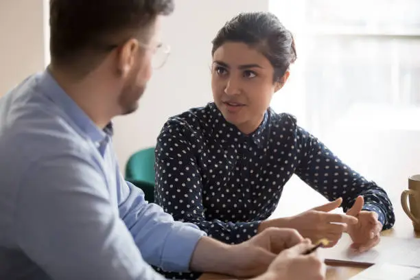 Photo of Indian female mentor worker talking to male coworker in office